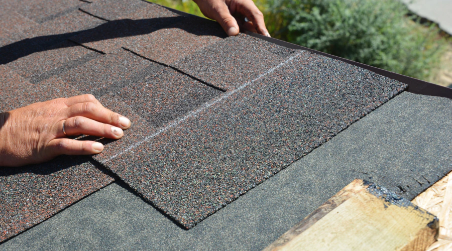 worker installing some asphalt roof tiles